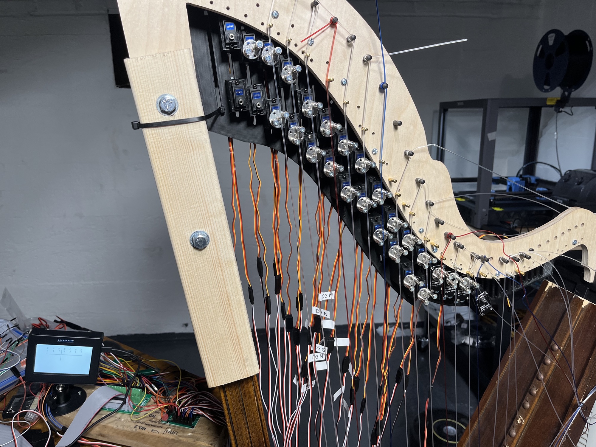 The full neck fitted with a long black 3D-printed bracket holding two rows of micro servos, with the servo wires tagged by note, such as C3 N and D3 S.